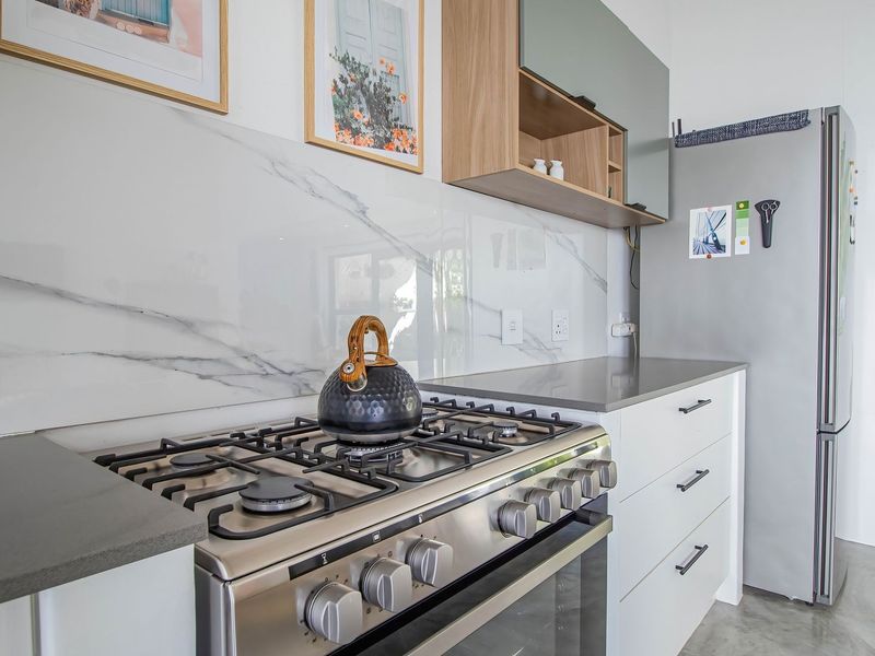 Modern kitchen featuring a stainless steel gas stove, marble-look splashback, stone countertops, and sleek white cabinetry with polished concrete flooring.
