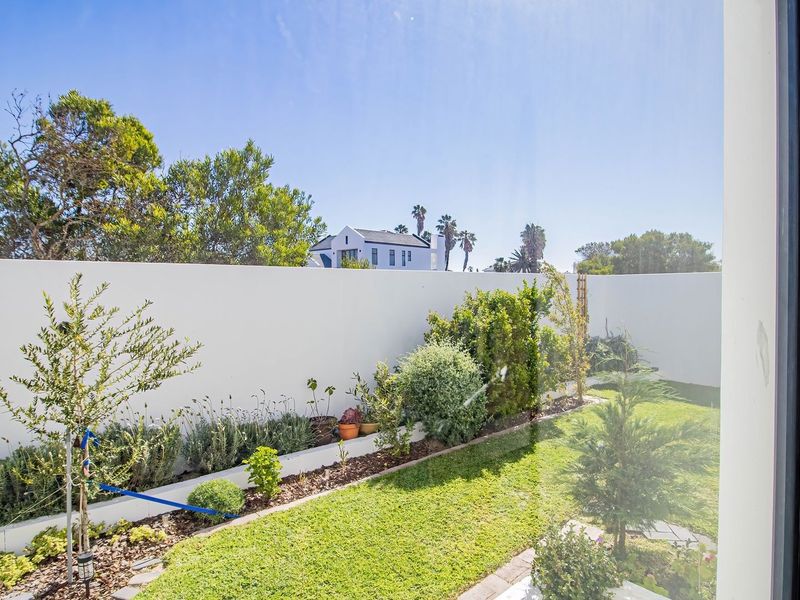 A well-maintained private garden featuring a manicured lawn, raised garden beds, and a clean boundary wall, viewed from an interior window.