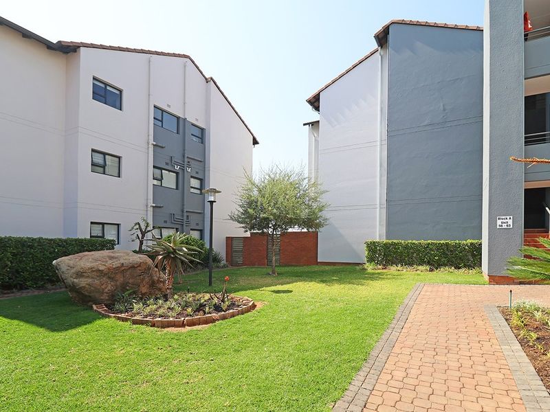 A well-maintained communal garden area between apartment blocks featuring a paved walkway, manicured lawn, and established landscaping.