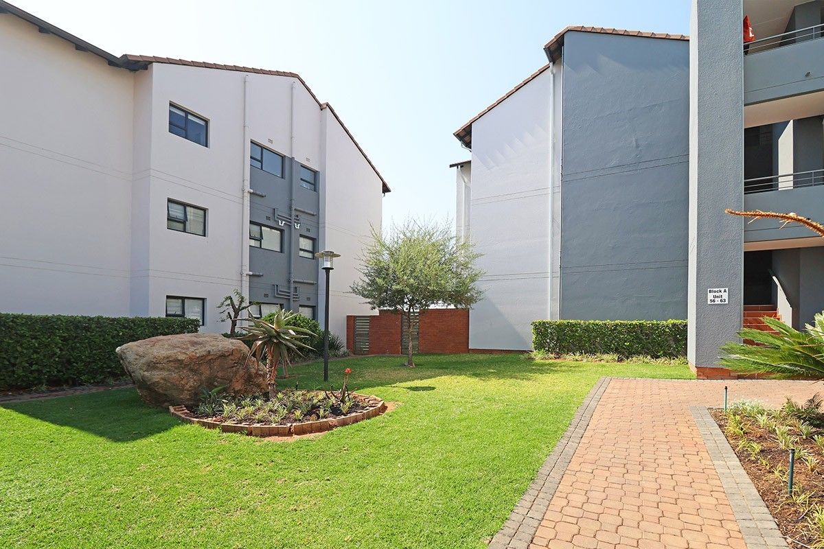 A well-maintained communal garden area between apartment blocks featuring a paved walkway, manicured lawn, and established landscaping.