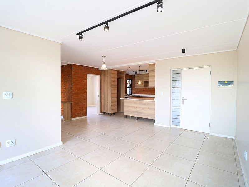 Spacious open-plan living and kitchen area featuring modern cabinetry, exposed brick accents, tiled flooring, and contemporary track lighting.