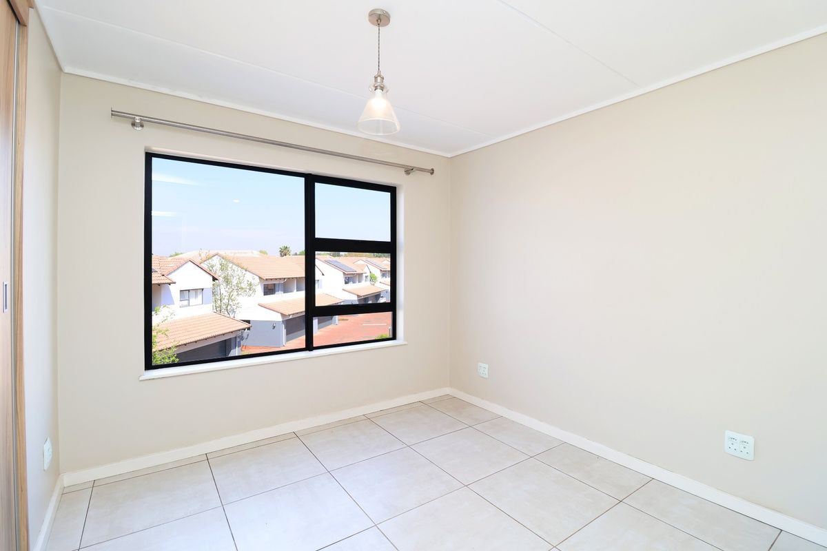 A bright, empty bedroom featuring neutral tiled flooring, a modern black-framed window, and a built-in cupboard, offering a clean and versatile living space.