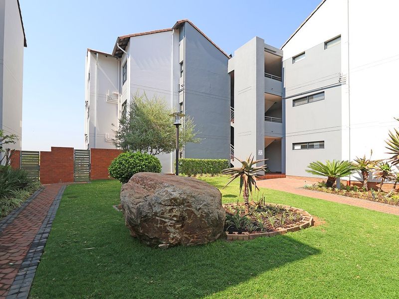 A well-maintained communal garden area featuring paved walkways, landscaped greenery, and access to the apartment building's exterior stairwell.