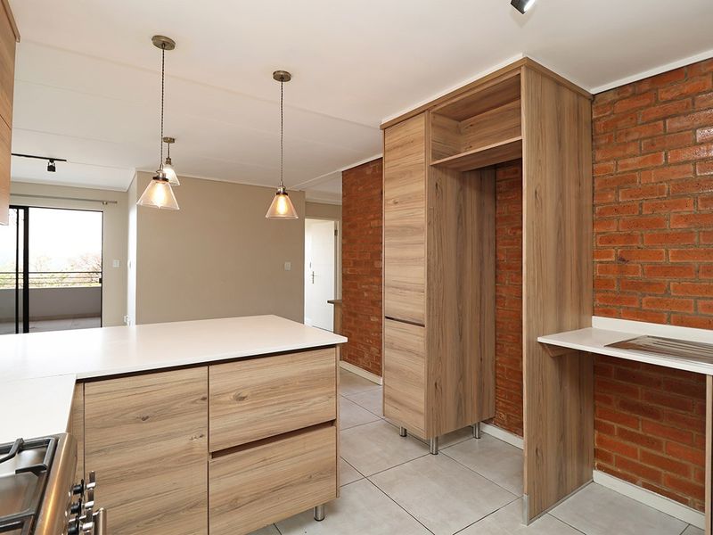 Modern kitchen featuring wood-finish cabinetry, stone countertops, a gas hob, and an exposed brick feature wall, offering a clean and contemporary aesthetic.