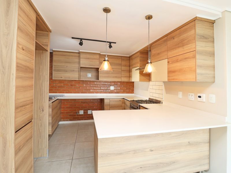 Modern kitchen featuring wood-look cabinetry, stone countertops, exposed brick accents, and integrated gas stove with stylish pendant and track lighting.