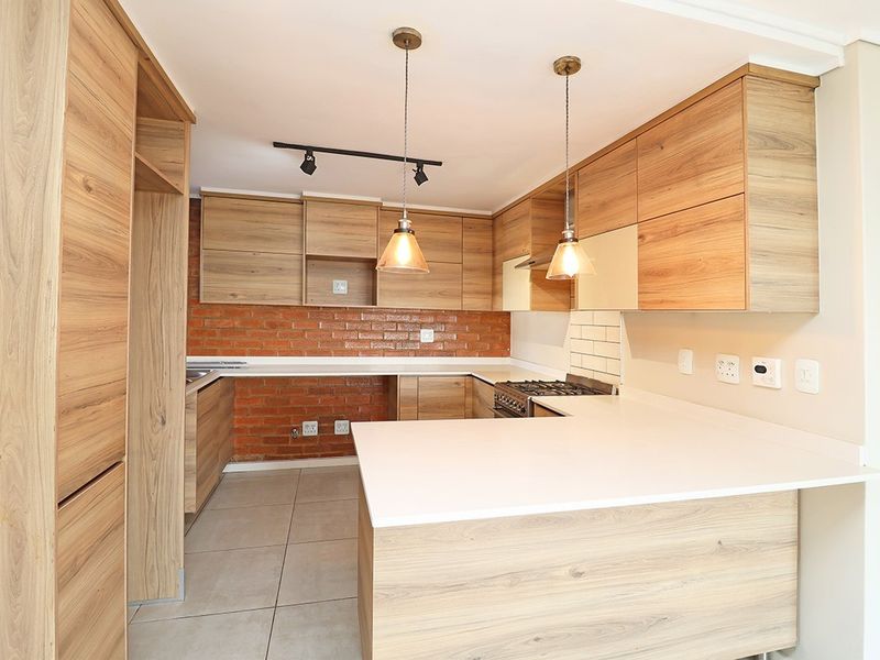 Modern kitchen featuring wood-look cabinetry, stone countertops, an exposed brick backsplash, and integrated gas stove with stylish pendant lighting.