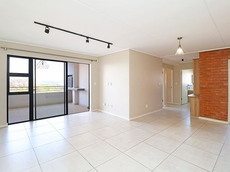 Spacious open-plan living area featuring neutral tiled floors, an exposed brick accent wall, and large sliding doors leading to a private balcony.