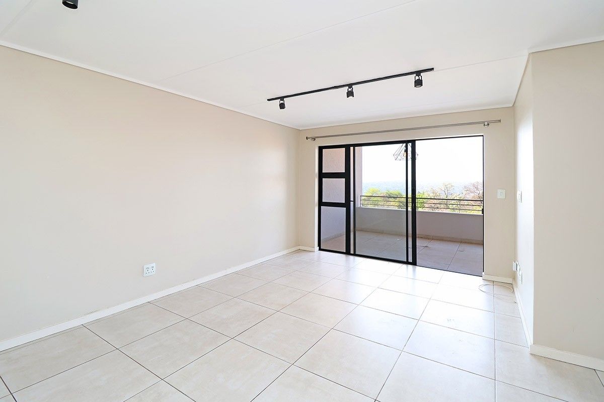 A bright, empty living room featuring neutral tiled flooring, modern track lighting, and large sliding glass doors leading to an outdoor balcony.