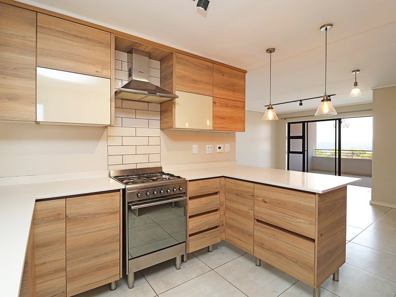 Modern kitchen featuring wood-look cabinetry, stone countertops, gas stove with extractor fan, and subway tile backsplash, flowing into an open-plan living area.