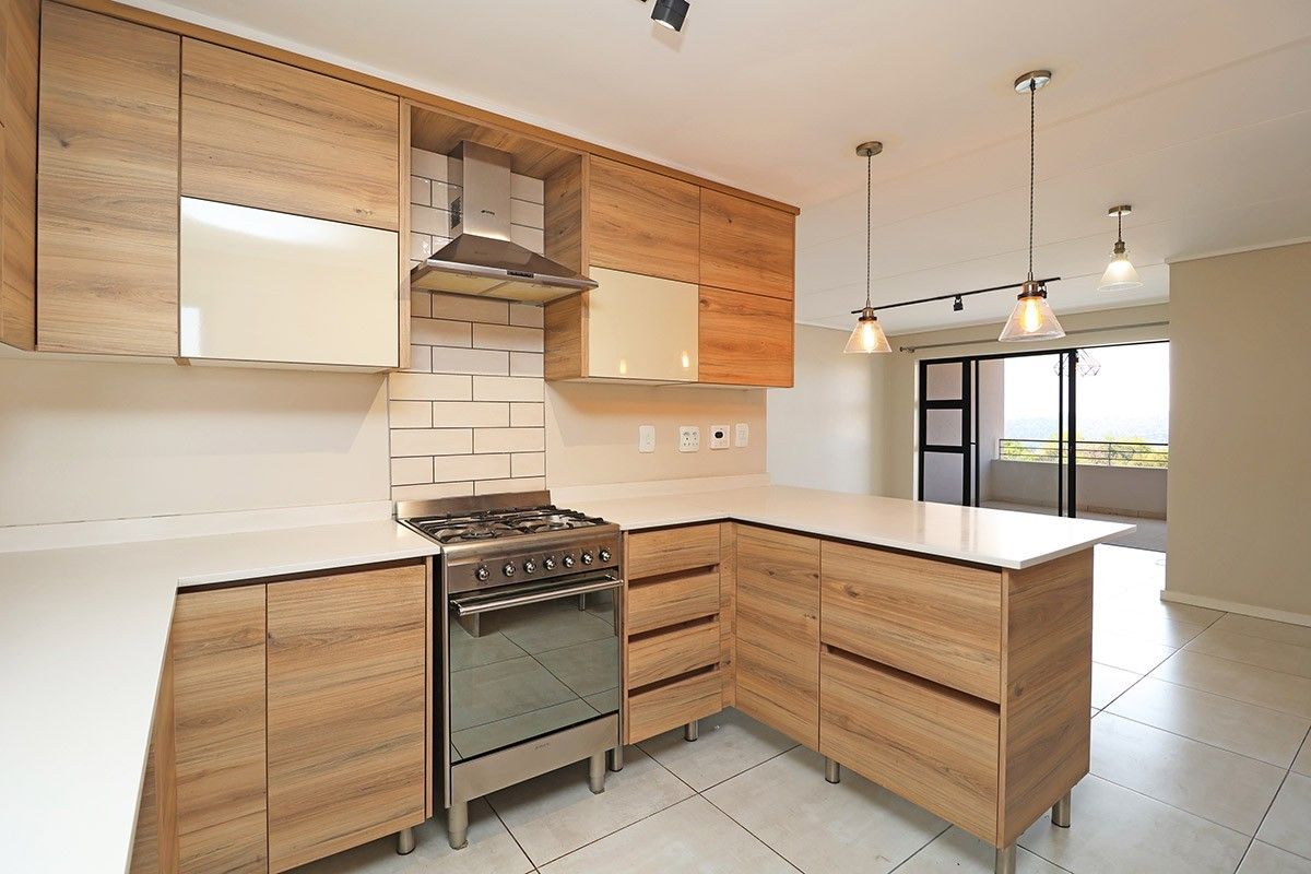 Modern kitchen featuring wood-look cabinetry, stone countertops, gas stove with extractor fan, and subway tile backsplash, flowing into an open-plan living area.