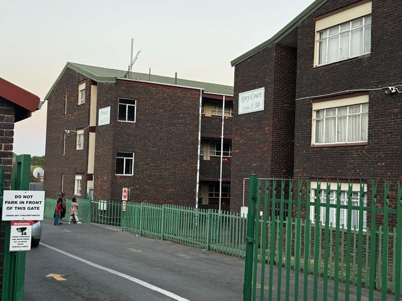 Exterior view of Spey Court apartment complex featuring face brick facade, secure gated entrance, and perimeter fencing.