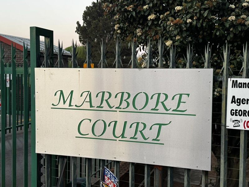 Entrance signage for Marbore Court apartment complex, featuring secure metal fencing and gate access.