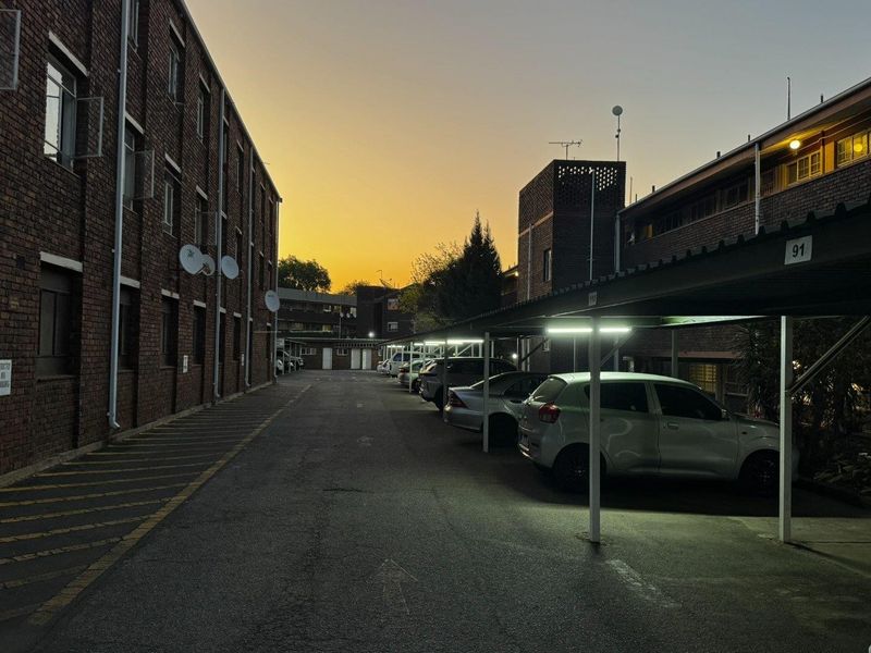Exterior view of an apartment complex parking area featuring brick building facades and covered parking bays at dusk.