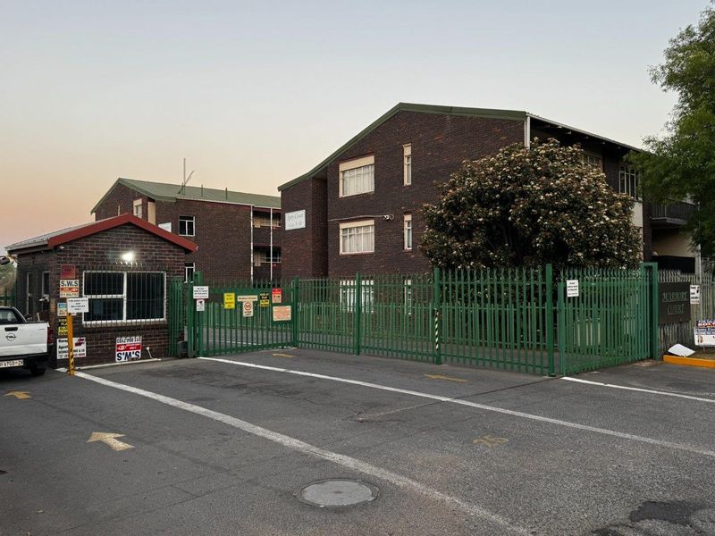 Front exterior view of Marbore Court apartment complex featuring a brick facade, secure gated entrance, and dedicated guard house.