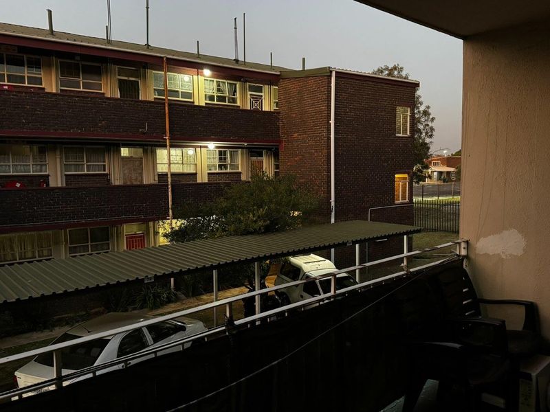 A view from a balcony overlooking the apartment complex courtyard, featuring a metal balustrade and views of the brick building exterior and parking area.