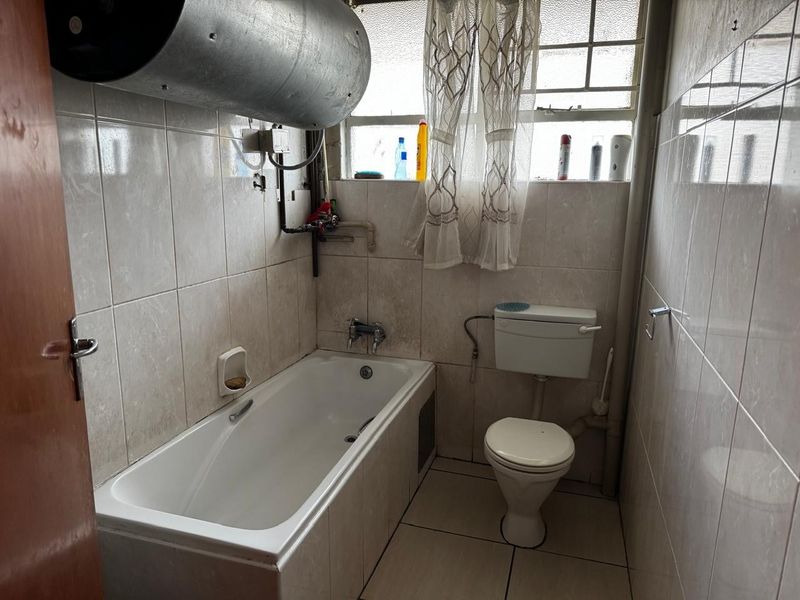 A functional bathroom featuring a bathtub, toilet, and tiled finishes, with an exposed water heater unit.
