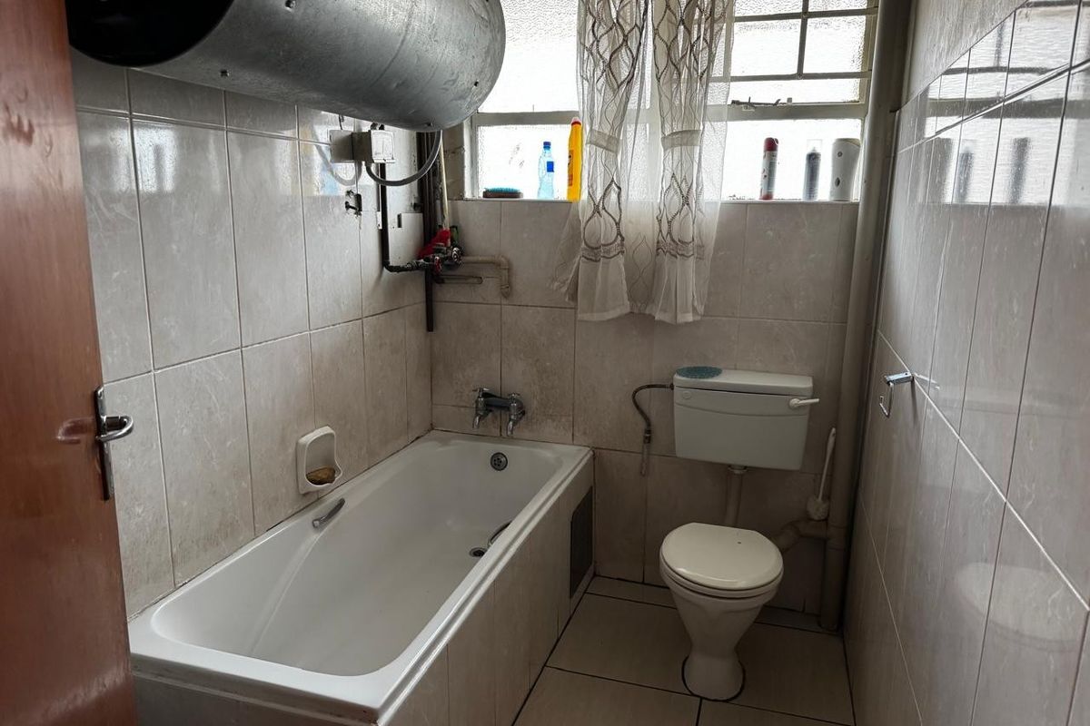 A functional bathroom featuring a bathtub, toilet, and tiled finishes, with an exposed water heater unit.