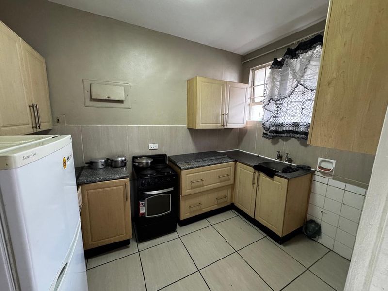 A functional kitchen featuring light wood cabinetry, granite countertops, a tiled backsplash, and a freestanding stove, offering potential for modernization.