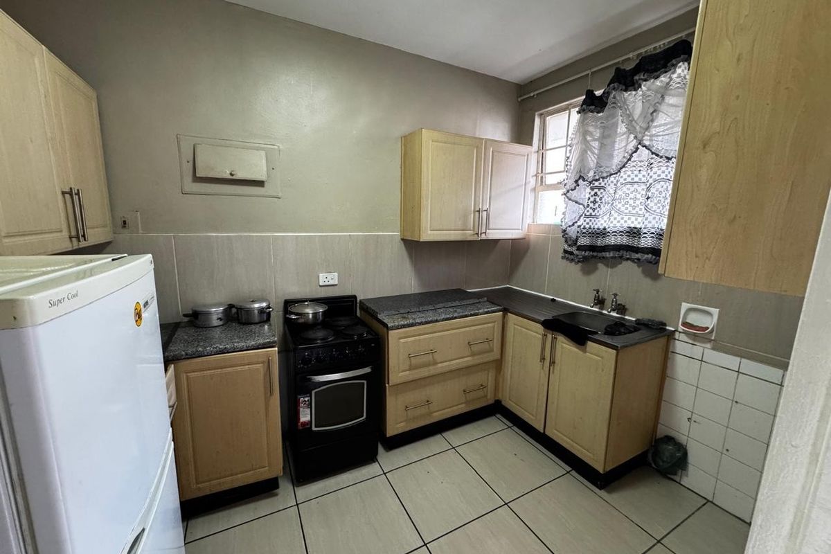 A functional kitchen featuring light wood cabinetry, granite countertops, a tiled backsplash, and a freestanding stove, offering potential for modernization.