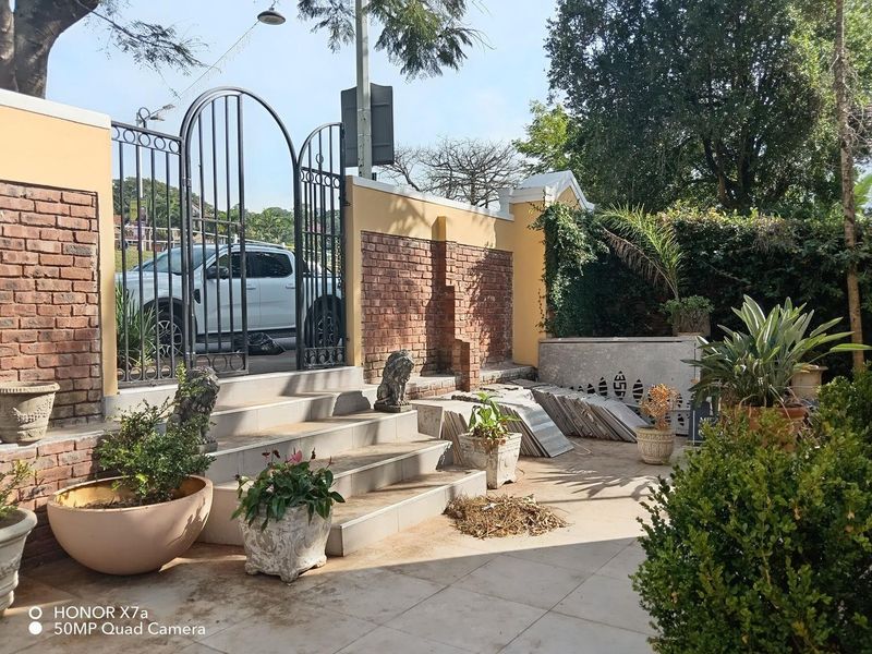 Front entrance area featuring a wrought iron gate, brick boundary wall, and tiled staircase leading to a paved outdoor space.