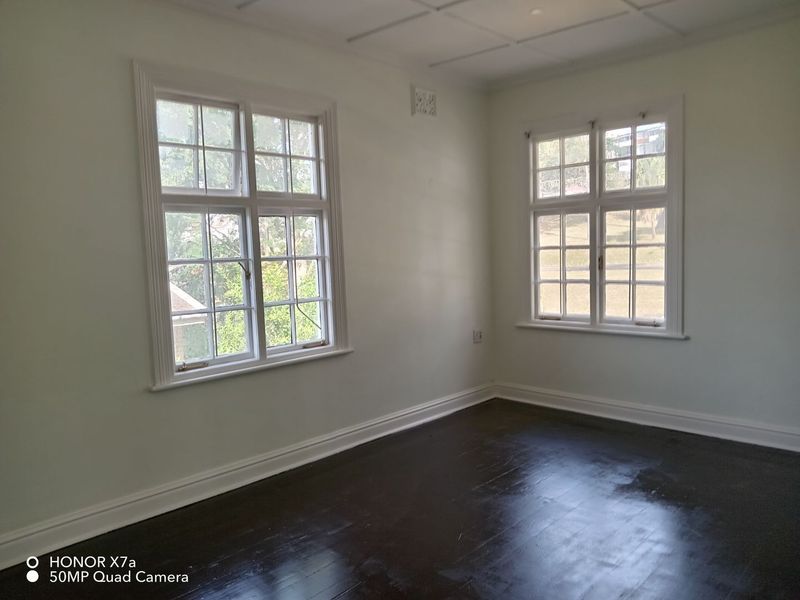 A bright, empty office space featuring dark timber flooring, classic multi-pane windows, and neutral walls, offering a versatile area for professional use.