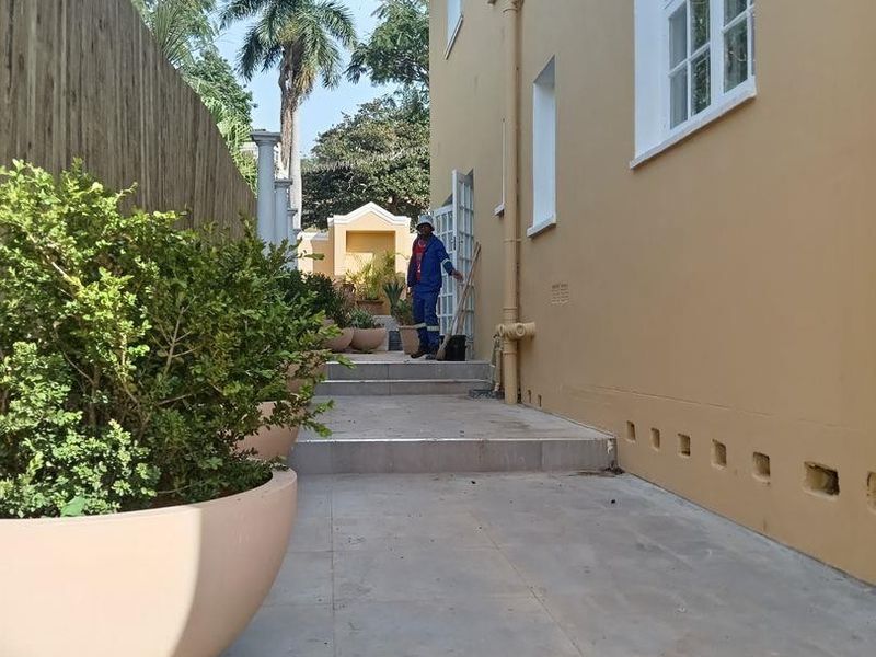A side exterior walkway featuring tiled steps, external plumbing, and a boundary fence along the side of the commercial building.