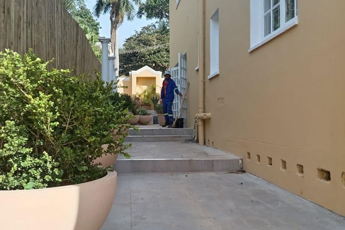 A side exterior walkway featuring tiled steps, external plumbing, and a boundary fence along the side of the commercial building.
