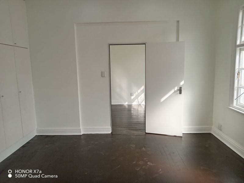 An empty bedroom featuring dark timber flooring, built-in cupboards, and a view into an adjacent room through an open doorway.
