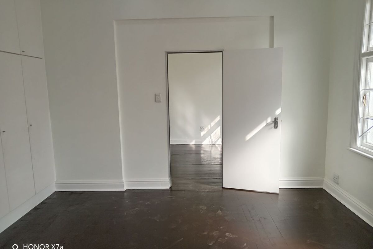 An empty bedroom featuring dark timber flooring, built-in cupboards, and a view into an adjacent room through an open doorway.