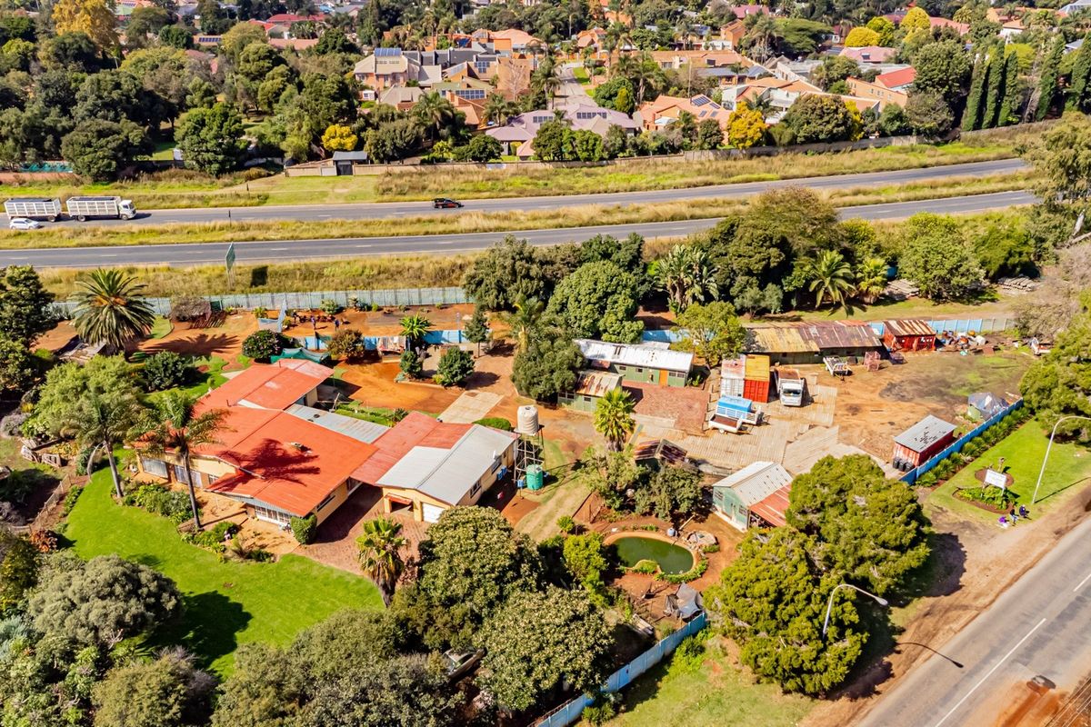 Aerial view of a small holding property featuring multiple outbuildings, a small pond, and extensive grounds situated near a main road.
