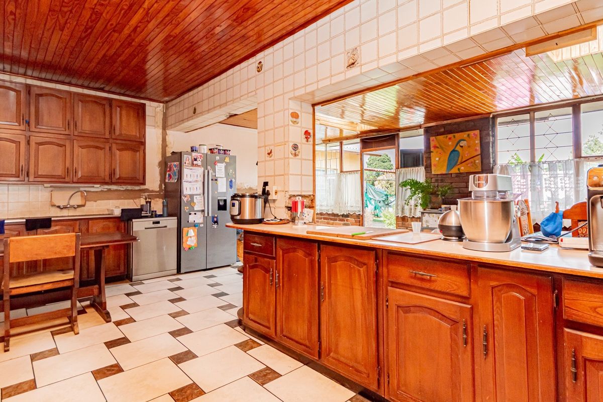 Spacious kitchen featuring traditional wooden cabinetry, a central island, tiled flooring, and a warm wooden ceiling, offering significant potential for modernization.