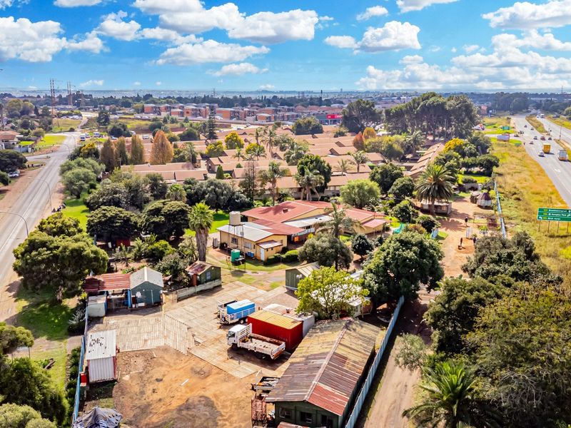 Aerial view of a small holding property featuring multiple outbuildings, corrugated metal roofs, and proximity to major road infrastructure.