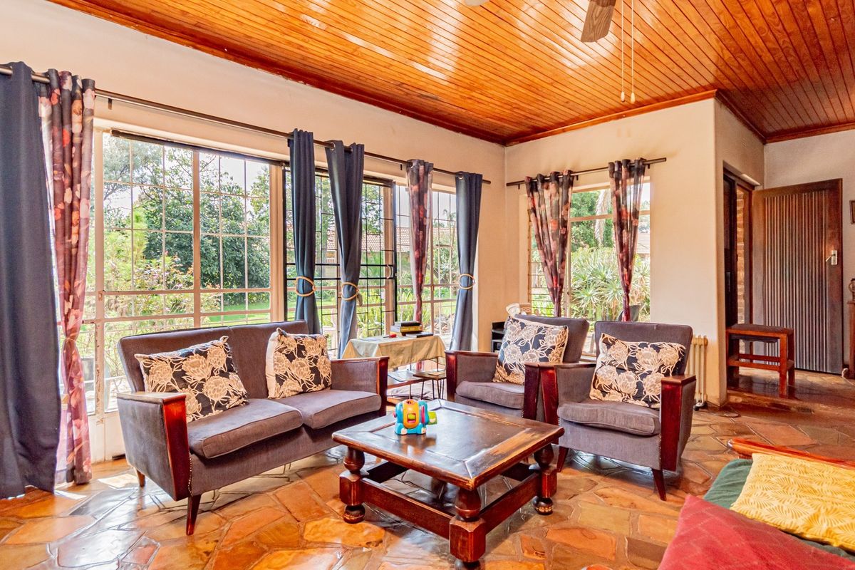 A sunlit living room featuring rustic flagstone flooring and a warm timber-clad ceiling, with large windows providing views of the garden.