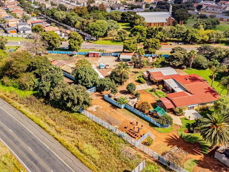 Aerial view of a small holding property featuring a main residence, outbuildings, mature landscaping, and perimeter fencing situated near a main road.