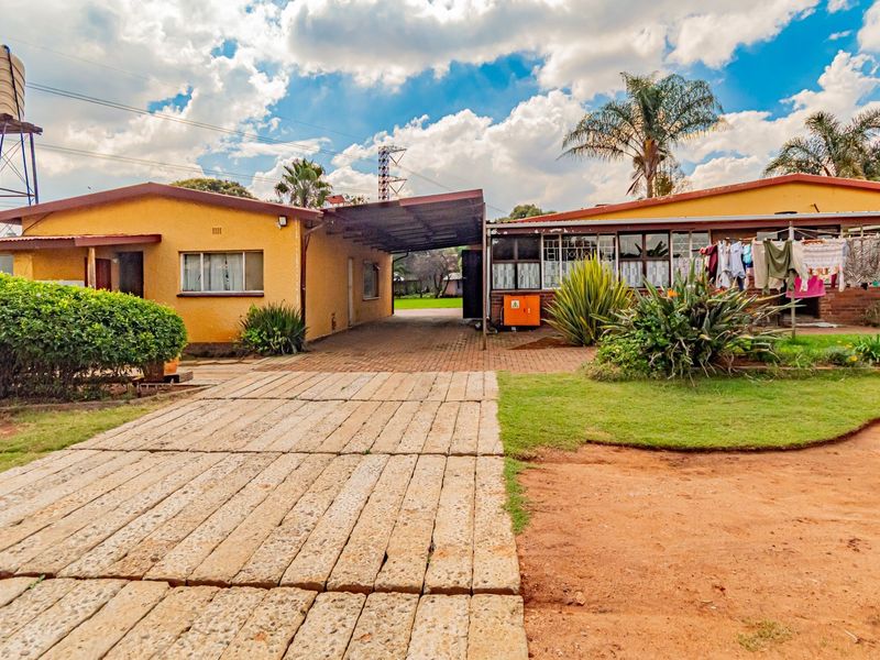 Front view of a small holding property featuring a paved driveway, carport, and elevated water tank, set within a spacious garden area.