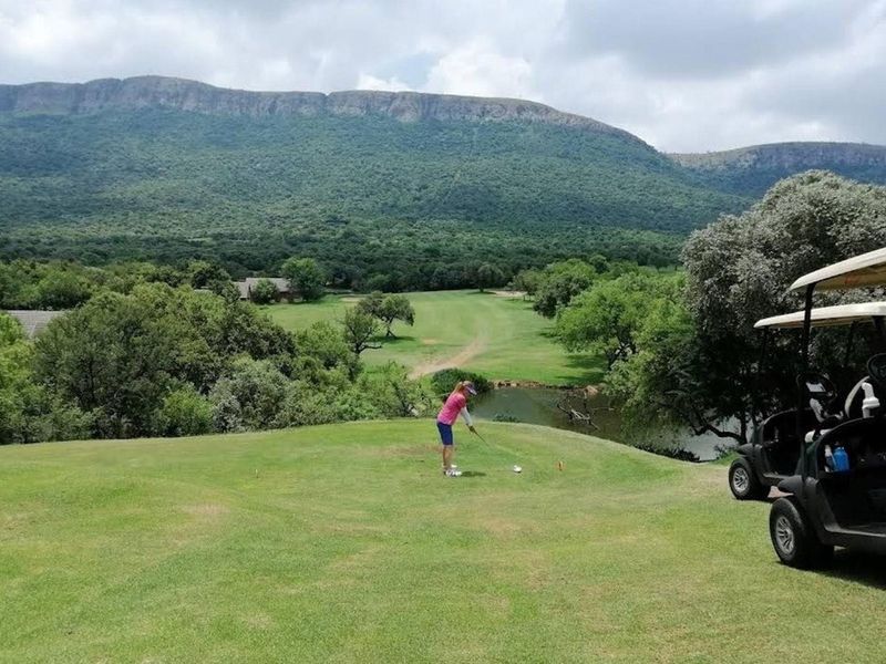 Scenic view of a golf course fairway, pond, and mountain landscape, showcasing the natural beauty of the surrounding estate.