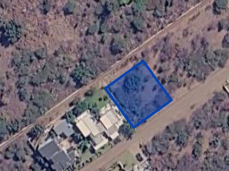 An aerial view showing a vacant residential land plot highlighted in blue, situated within a natural, undeveloped landscape.