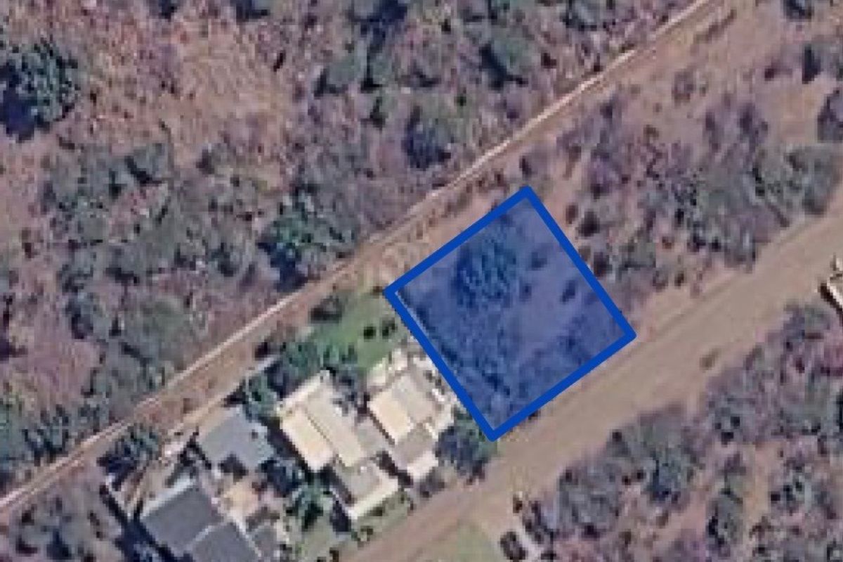 An aerial view showing a vacant residential land plot highlighted in blue, situated within a natural, undeveloped landscape.