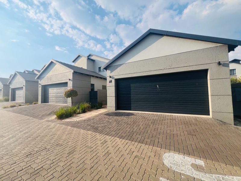 Front view of a modern townhouse complex featuring paved driveways and automated garage doors with a clean, contemporary architectural finish.