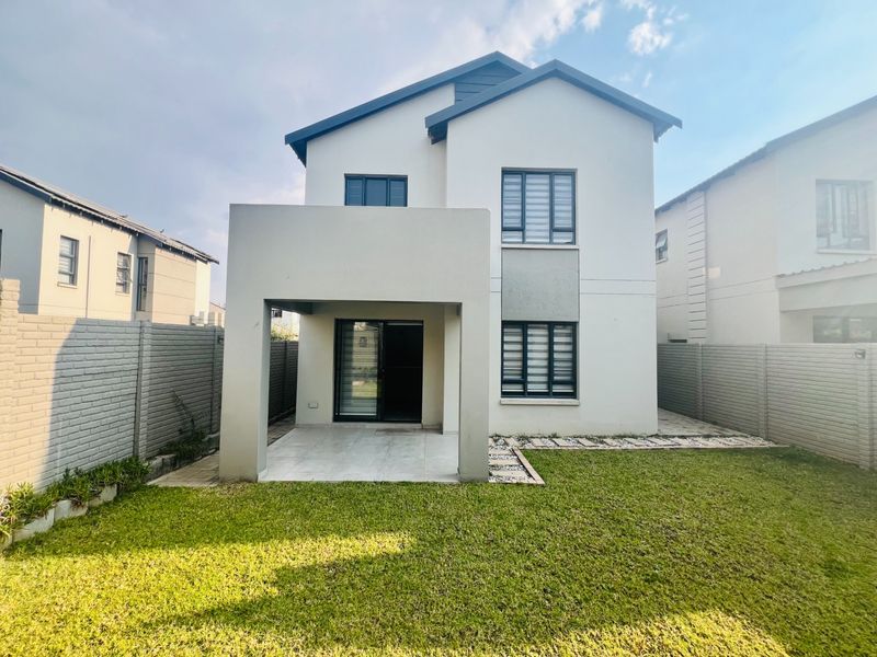 Rear view of a modern double-story townhouse featuring a covered patio, tiled flooring, sliding glass doors, and a well-maintained private garden with boundary walls.