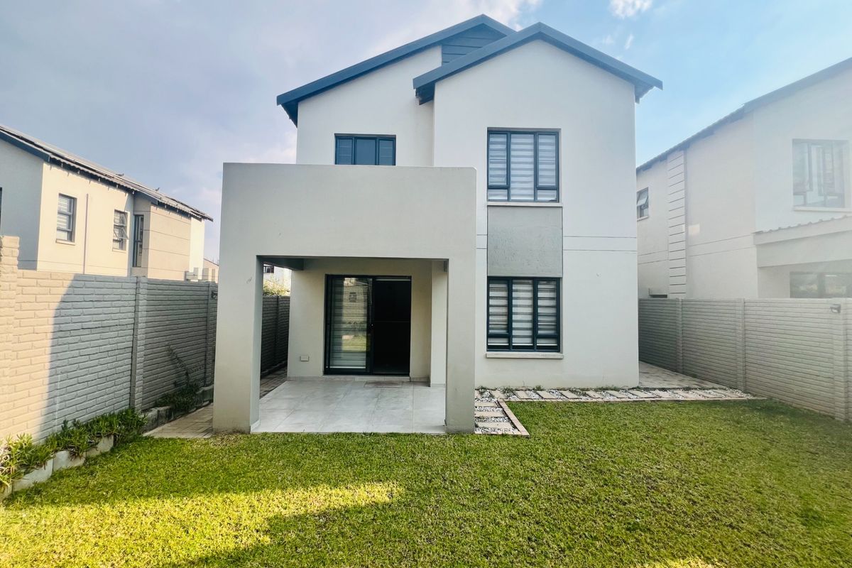 Rear view of a modern double-story townhouse featuring a covered patio, tiled flooring, sliding glass doors, and a well-maintained private garden with boundary walls.