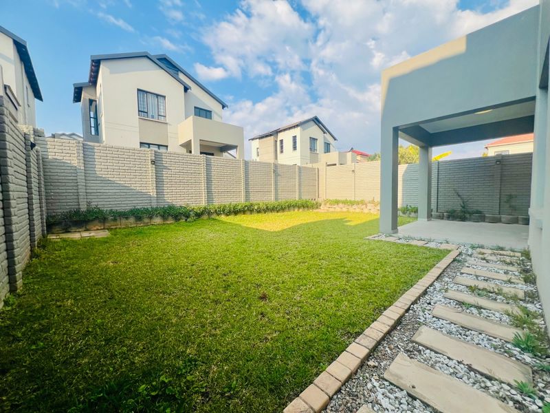 A private rear garden featuring a well-maintained lawn, a covered patio area, and a paved walkway enclosed by high brick boundary walls.