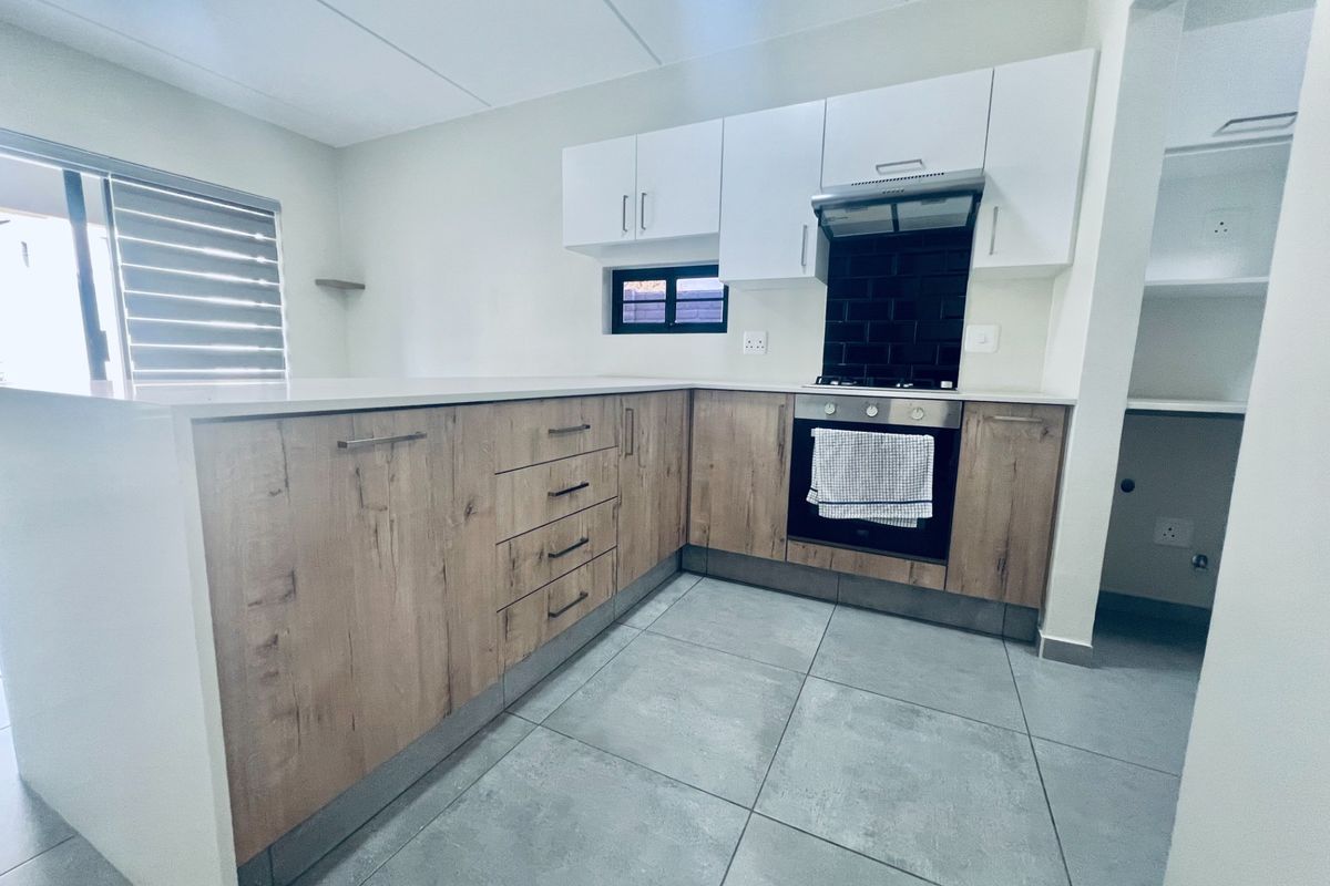 Modern kitchen featuring wood-look lower cabinetry, white upper cabinets, stone countertops, subway tile backsplash, and integrated oven with extractor fan.