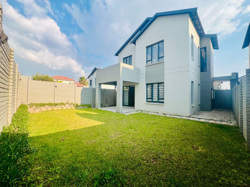 Rear view of the townhouse featuring a covered patio, private garden with lawn, and secure brick boundary walls.