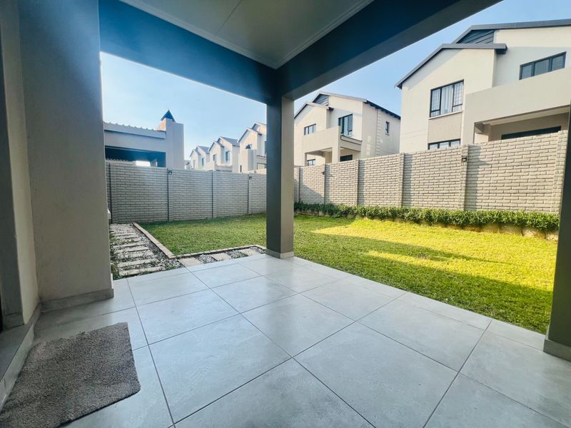 A spacious covered patio featuring large format floor tiles, overlooking a private garden with a well-maintained lawn and secure brick boundary walls.