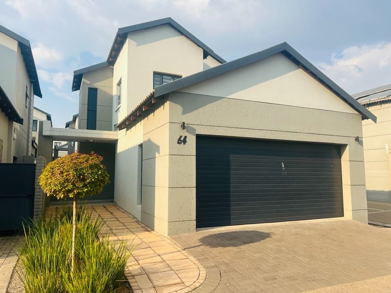 Front elevation of a modern townhouse featuring a double garage, paved driveway, and a neat tiled walkway leading to the entrance.
