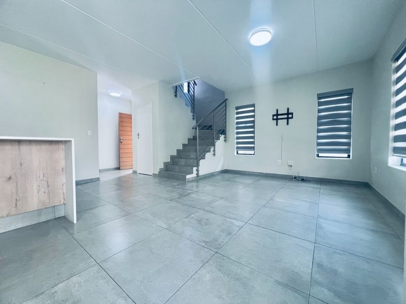Spacious open-plan living area featuring modern grey floor tiles, a staircase with a metal balustrade, and neutral finishes throughout.