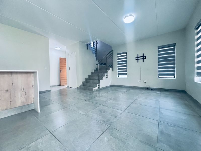 Spacious open-plan living area featuring large format floor tiles, a modern staircase with metal balustrade, and neutral finishes throughout.
