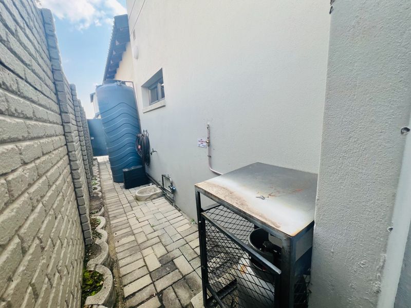 Side utility area featuring a water storage tank, paved walkway, and a secure gas cylinder storage cage.
