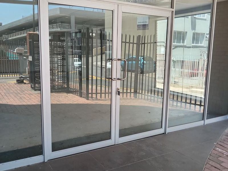 Commercial entrance featuring aluminium-framed glass double doors and large storefront windows with tiled flooring, providing clear visibility into the premises.